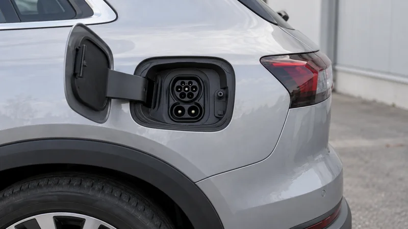 Geöffneter Ladeanschluss an der hinteren Seitenwand eines silbernen Elektroautos.